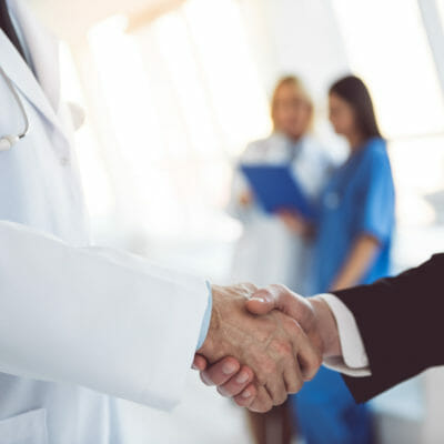 Cropped image of handsome mature doctor and young businessman shaking hands while standing in the hospital hall